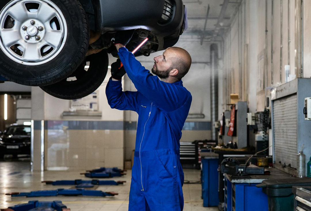 Mechanic in blue overalls inspecting car undercarriage for full annual service safety