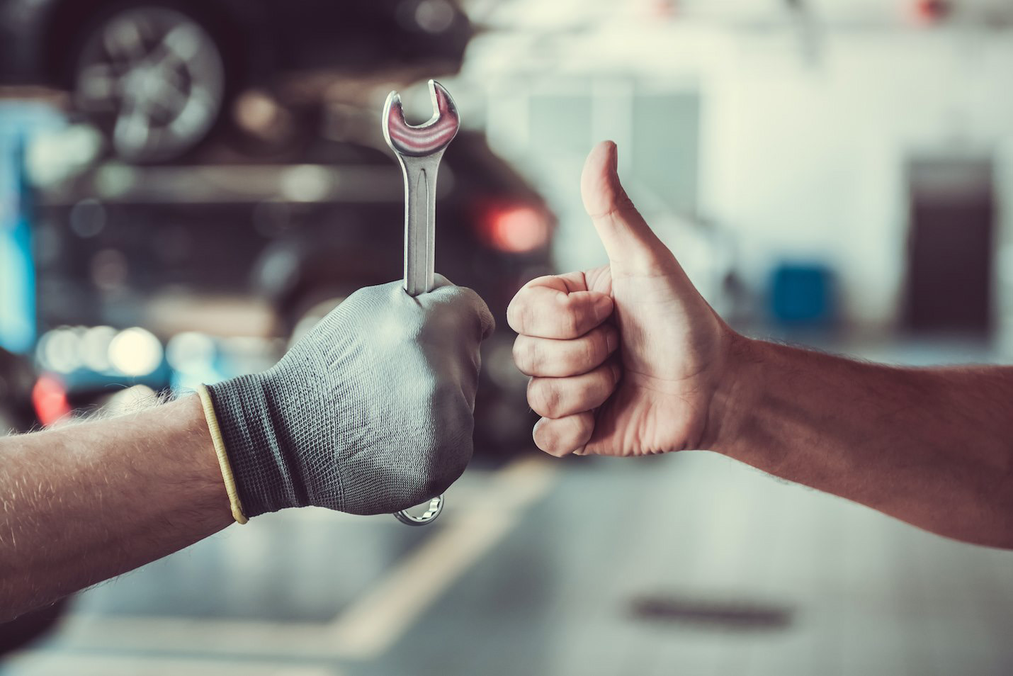 Close-up of mechanic holding a spanner with a thumbs up for reliable car service