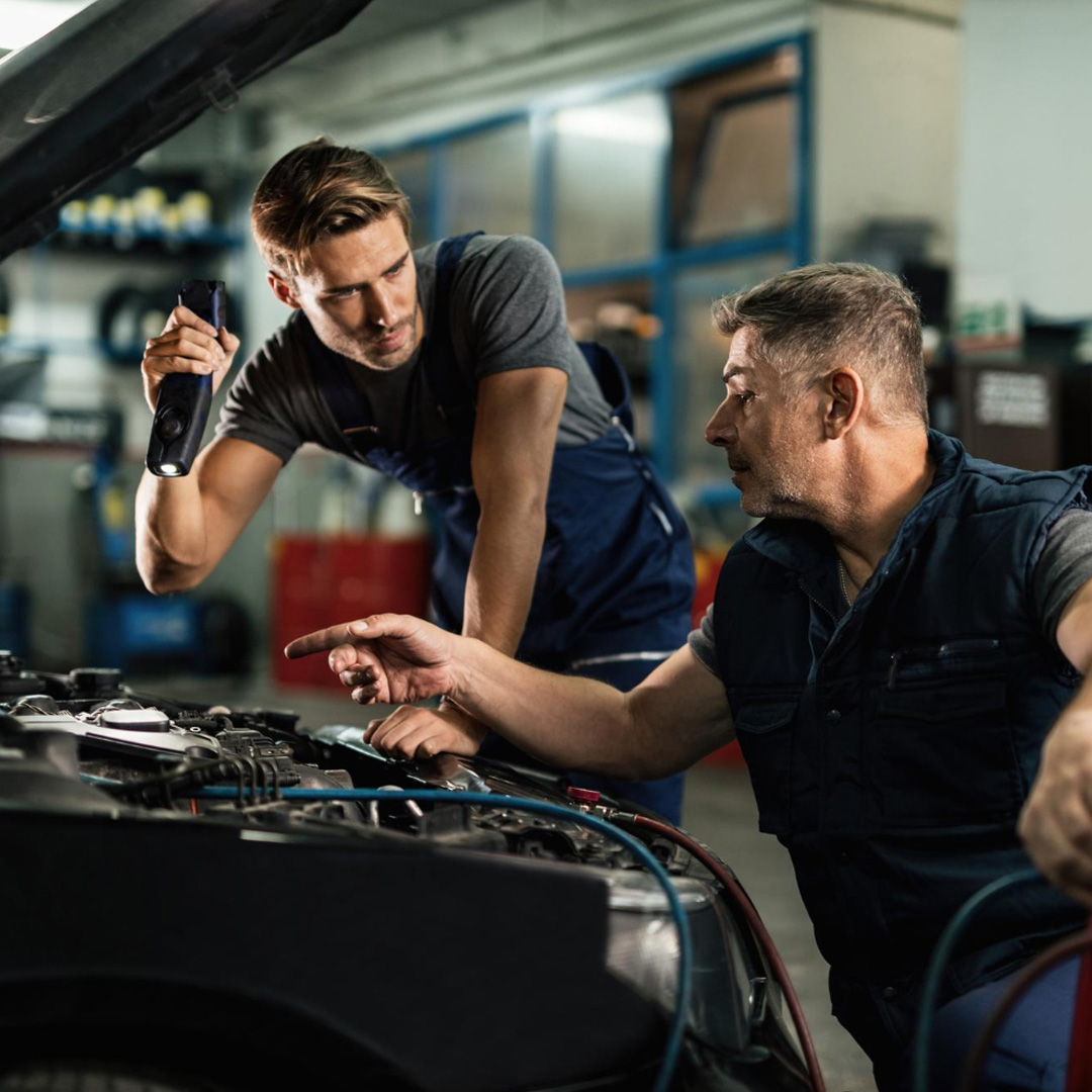 Two experienced mechanics working together on a car engine in the Hildenborough workshop.